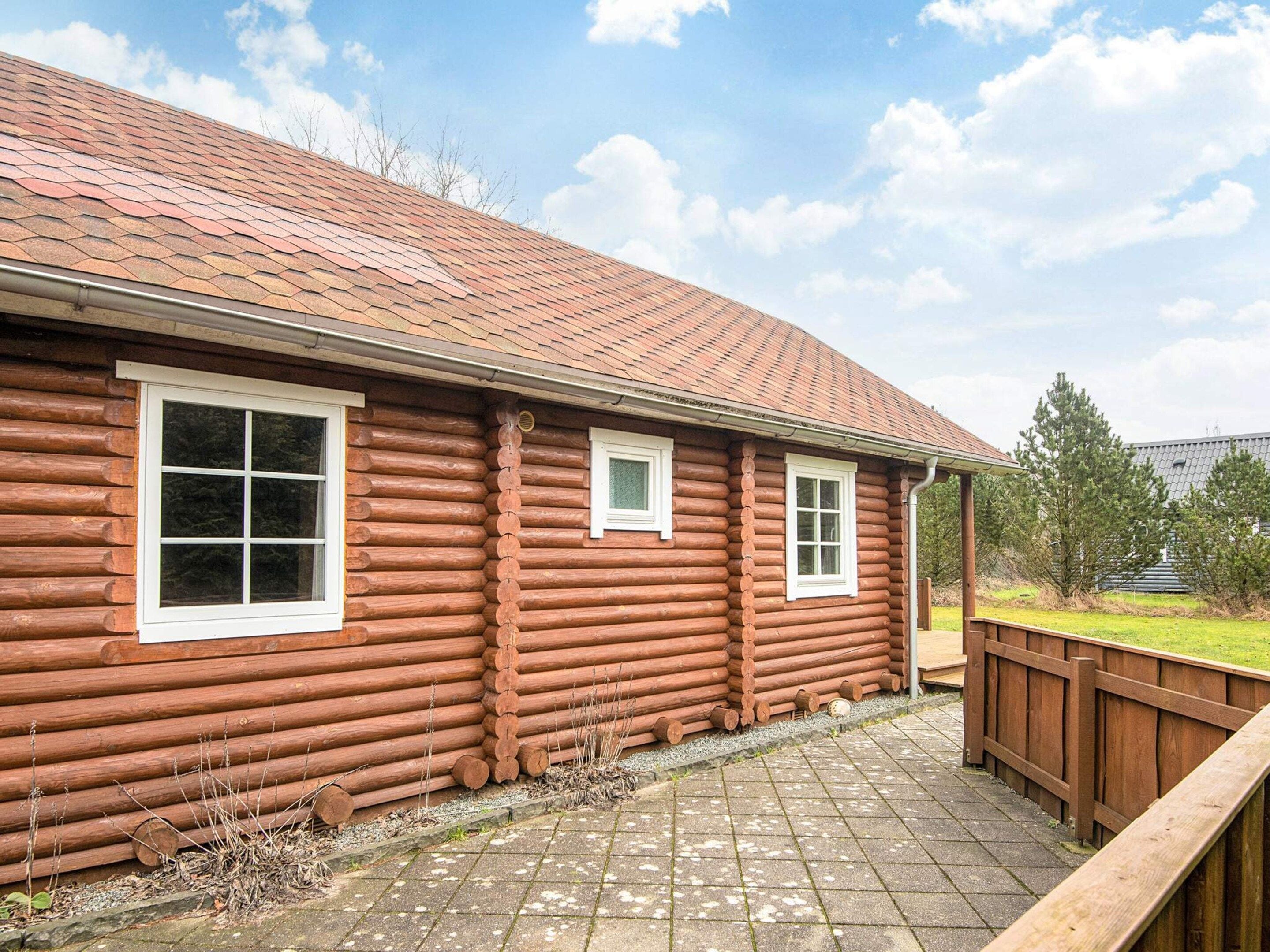 A log cabin with a tiled roof, a wooden deck, and a fenced yard.