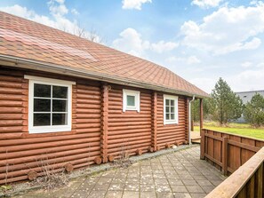 A log cabin with a tiled roof, a wooden deck, and a fenced yard. - 6 Person Holiday Home in Hovborg (Hovborg)