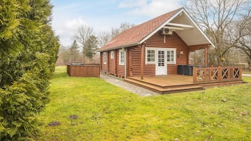 A log cabin with a wooden deck, a hot tub, and a covered porch.