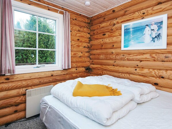 Acogedora habitación de cabaña con cama, ventana con cortinas, radiador y un cuadro enmarcado en la pared.