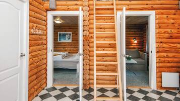 A log cabin-style room with a checkered floor, a bed, a desk, and a ladder leading to a loft area with wooden crates.