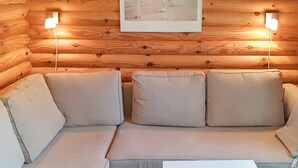 L'intérieur d'un chalet en bois, avec un canapé et deux lampes fixées au mur.