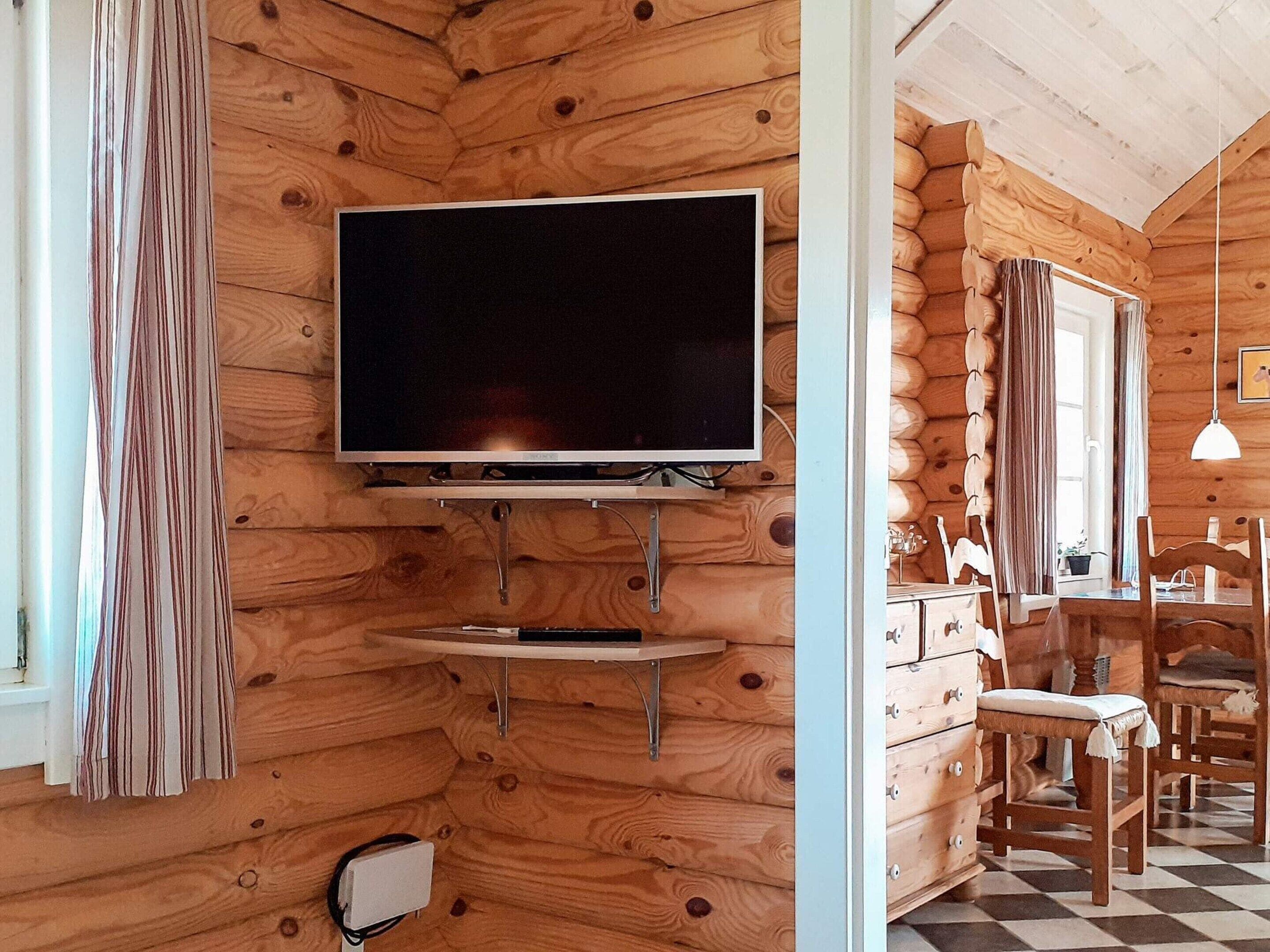 A log cabin interior with a mounted flat-screen TV, wooden furniture, and a checkered floor.