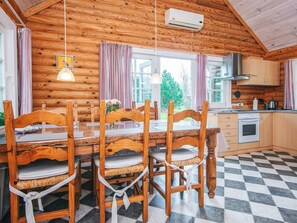 A wooden cabin interior with a dining table, chairs, a kitchen area, and a view of the outdoors. - 6 Person Holiday Home in Hovborg (Hovborg)