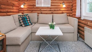 L’intérieur chaleureux d’un chalet avec un canapé d’angle beige, une petite table blanche et des murs en bois.