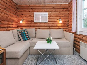 A cozy cabin interior with a beige sectional sofa, a small white table, and wooden walls. - 6 Person Holiday Home in Hovborg (Hovborg)
