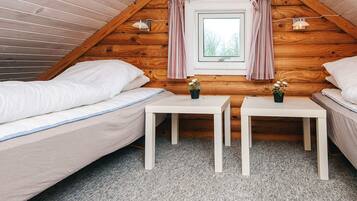 A cozy attic bedroom with two beds, a small window with curtains, and a table with a plant.