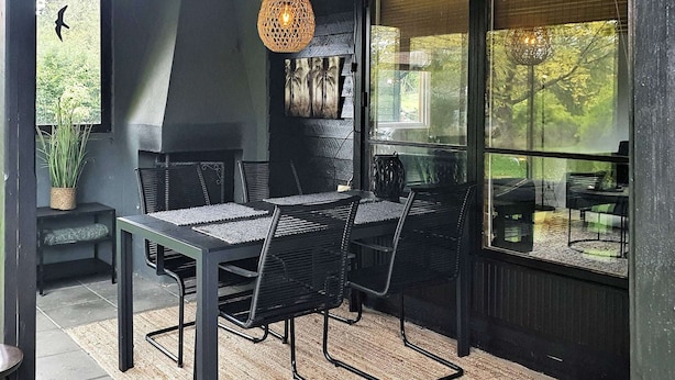 Een eethoek binnen met een tafel, stoelen, een hanglamp en een uitzicht door grote ramen.