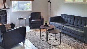 Een woonkamer met een bank, fauteuil en een bijzettafeltje met een plant.