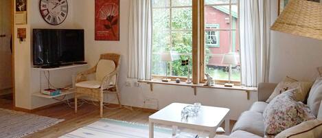 Una sala de estar con televisión, una silla, un sofá, una mesa de centro y una ventana con cortinas.