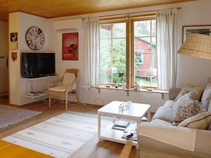 Una sala de estar con televisión, una silla, un sofá, una mesa de centro y una ventana con cortinas.