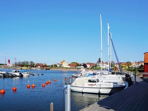 Un puerto deportivo con barcos amarrados, un faro y casas al fondo.