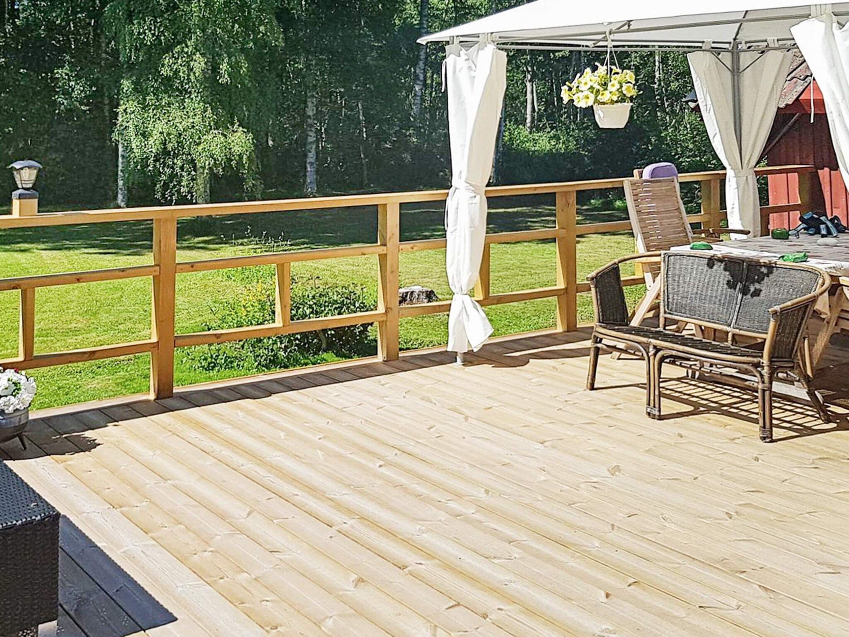 A wooden deck with a table and chairs, a white canopy, and a view of a green lawn.