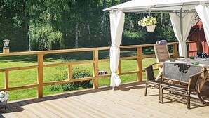 Une terrasse en bois avec une table et des chaises, un auvent blanc et une vue sur une pelouse verdoyante.
