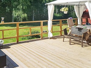 Una terraza de madera con una mesa y sillas, un dosel blanco y vista a un c ésped verde.