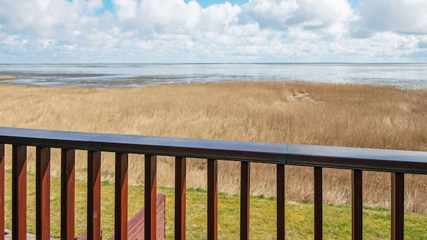 Blick auf einen Strand von einer Holzdielenveranda mit Geländer.