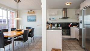 Eine moderne Küche mit einem Edelstahl-Kühlschrank, einem Einbauofen und einem Gasherd. Es gibt eine Essecke mit einem Holztisch und Stühlen sowie einen kleinen Holzschemel.
