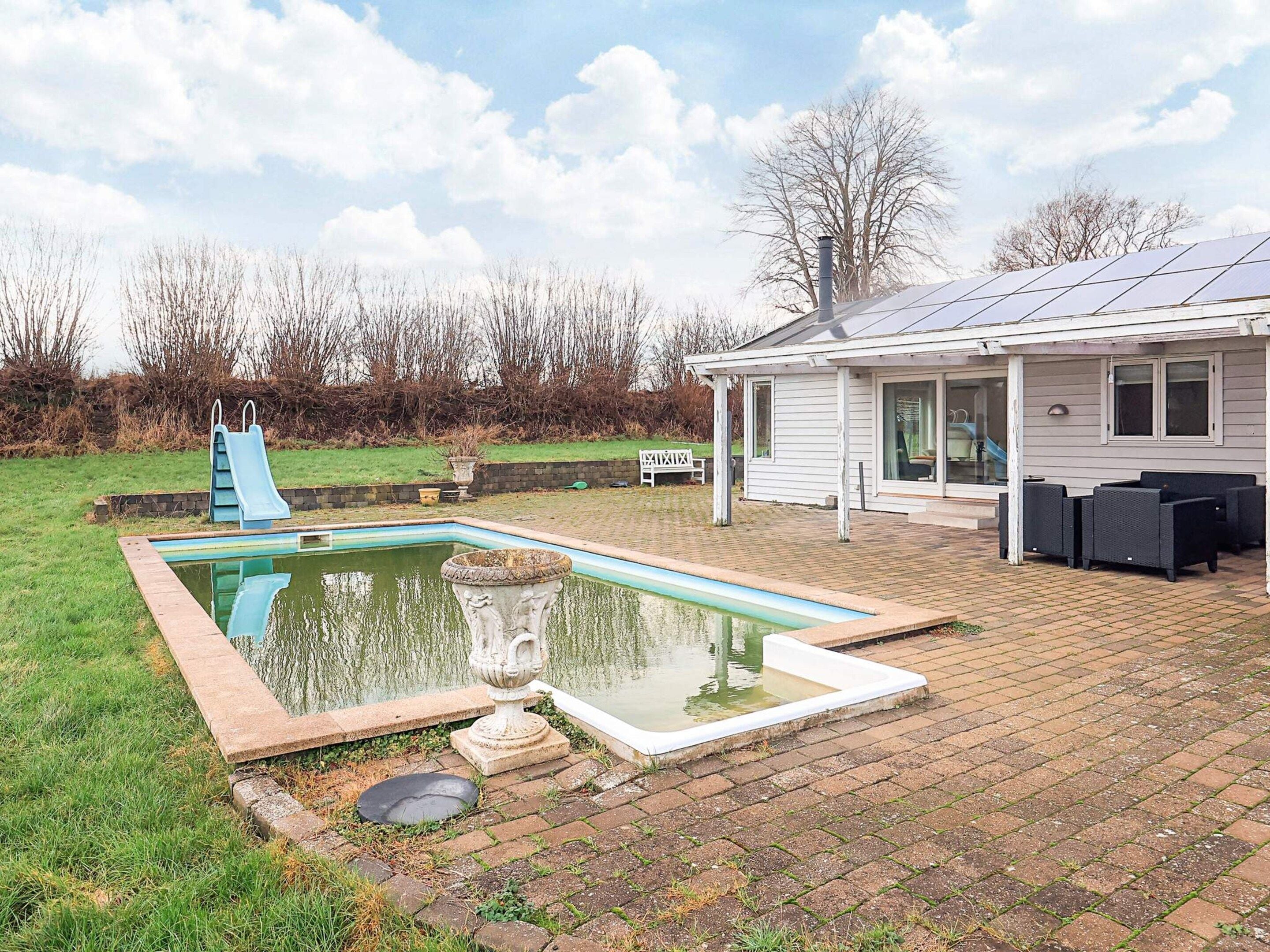 Una piscina con tobogán, un patio con mobiliario exterior y una casa con paneles solares.