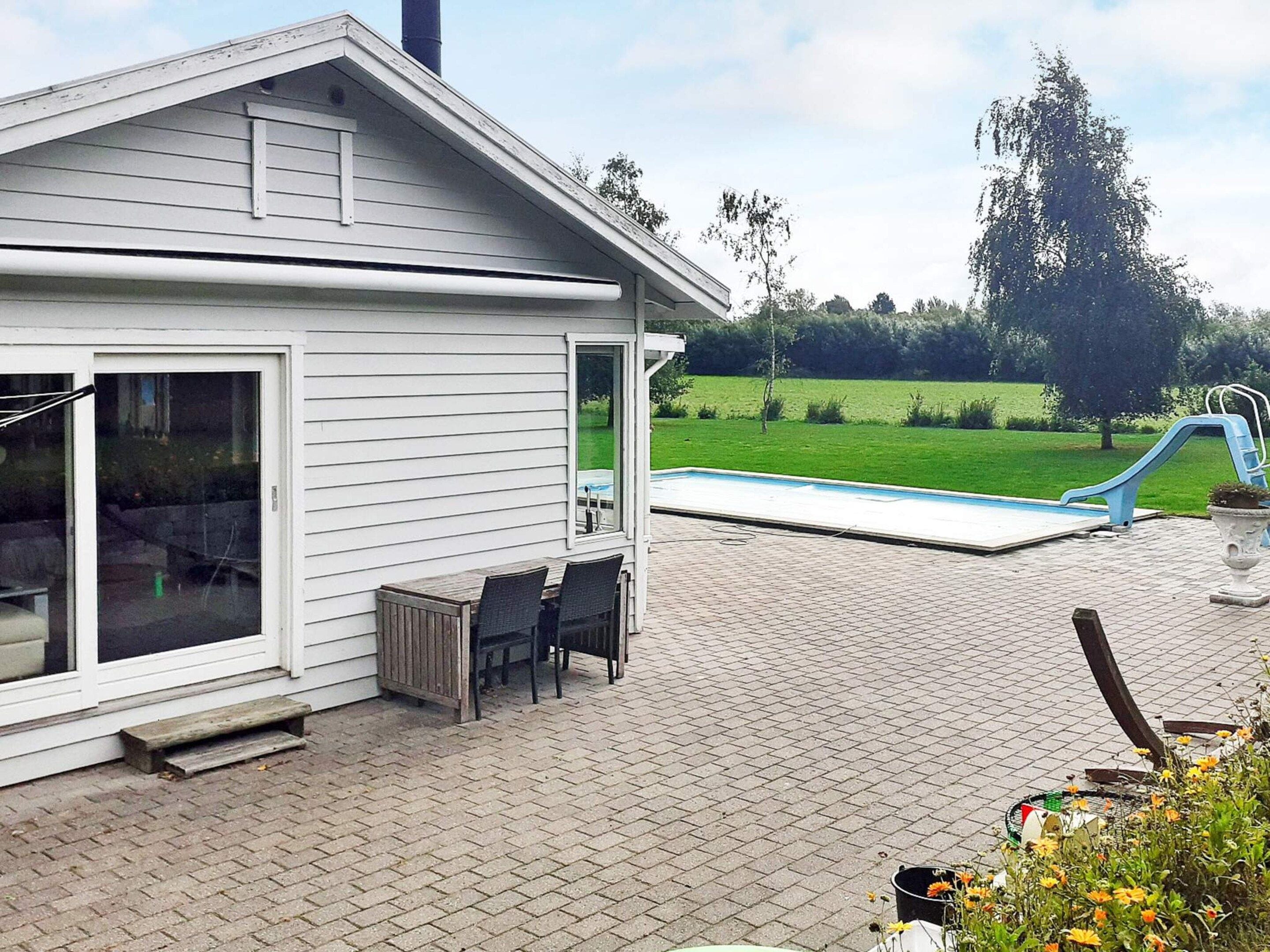 Una casa con patio, piscina y un área verde al fondo.