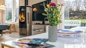 A modern living room with a fireplace, a television, and a vase of flowers on a table. - 4 Star Holiday Home in Rodvig Stevns (Rodvig Stevns)