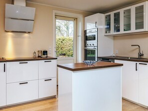 A modern kitchen with white cabinetry, a central island, and a built-in oven. - 4 Star Holiday Home in Rodvig Stevns (Rodvig Stevns)
