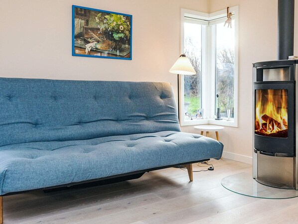 A modern living room with a blue sofa, a painting on the wall, a window with a view, and a wood-burning stove.