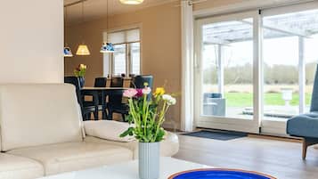 A living room with a sofa, a coffee table with a vase of flowers, and a dining area in the background.