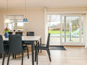 A dining area with a table and chairs, a vase with flowers, and a view of a park through a glass door. - 4 Star Holiday Home in Rodvig Stevns (Rodvig Stevns)