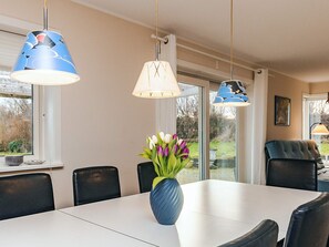 A dining area with a white table, black chairs, and a vase with flowers. There are three hanging lamps with different designs. - 4 Star Holiday Home in Rodvig Stevns (Rodvig Stevns)