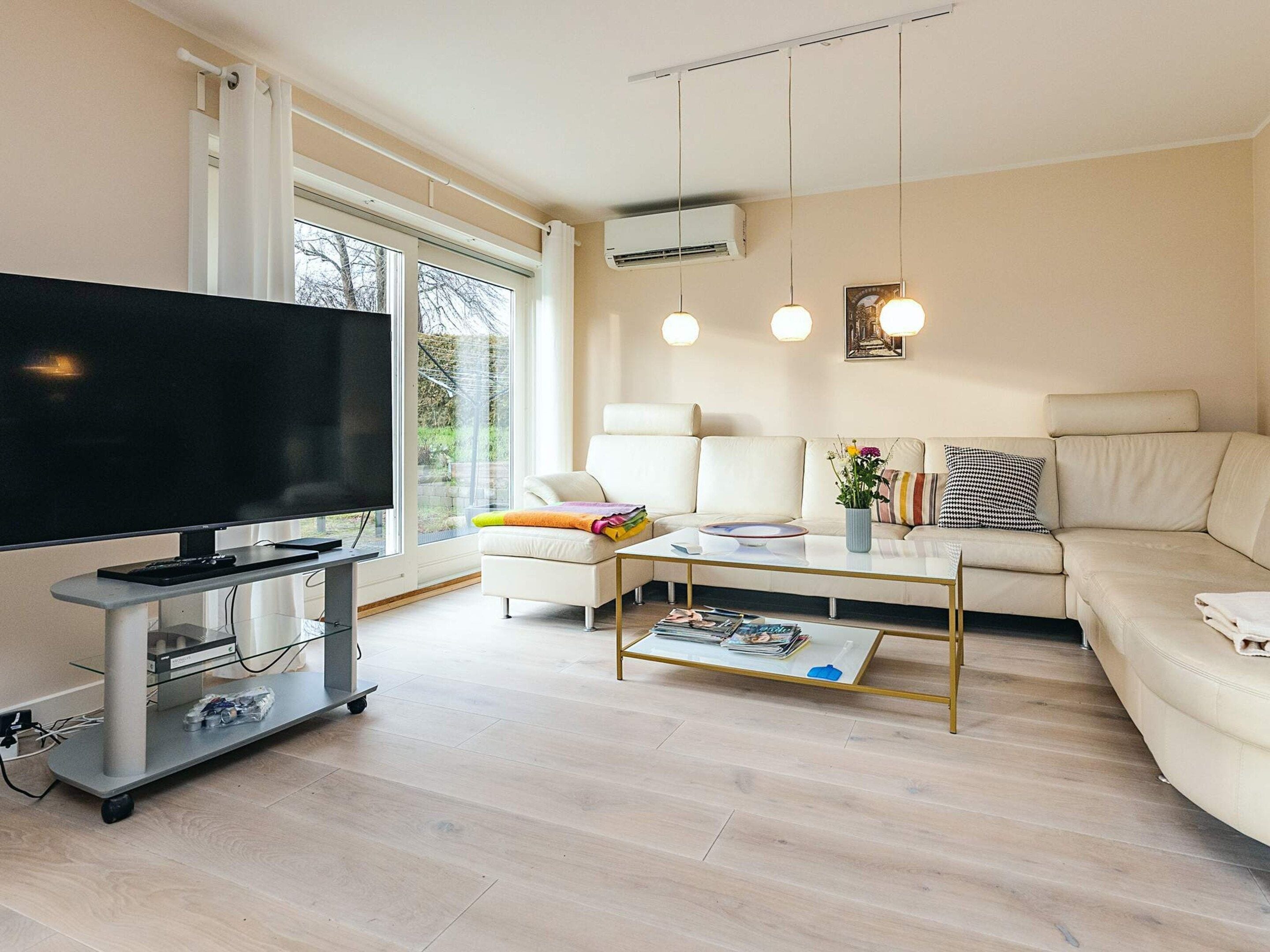 Una sala de estar moderna con un televisor de pantalla plana, un sofá, una mesa de centro e iluminación colgante.