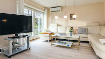 Una sala de estar moderna con un televisor de pantalla plana, un sofá, una mesa de centro e iluminación colgante.