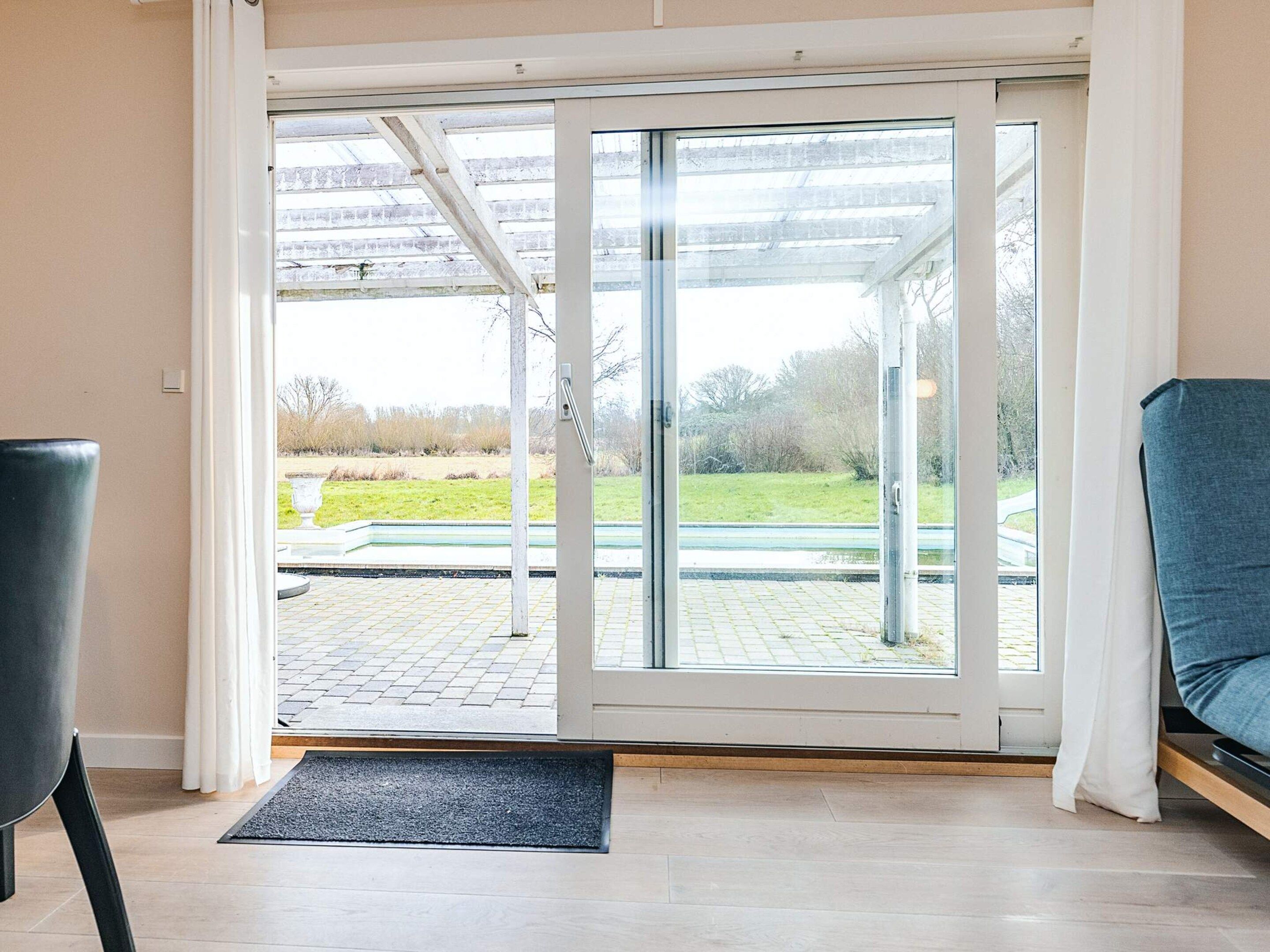 A room with a sliding glass door leading to an outdoor area with a paved walkway and greenery.