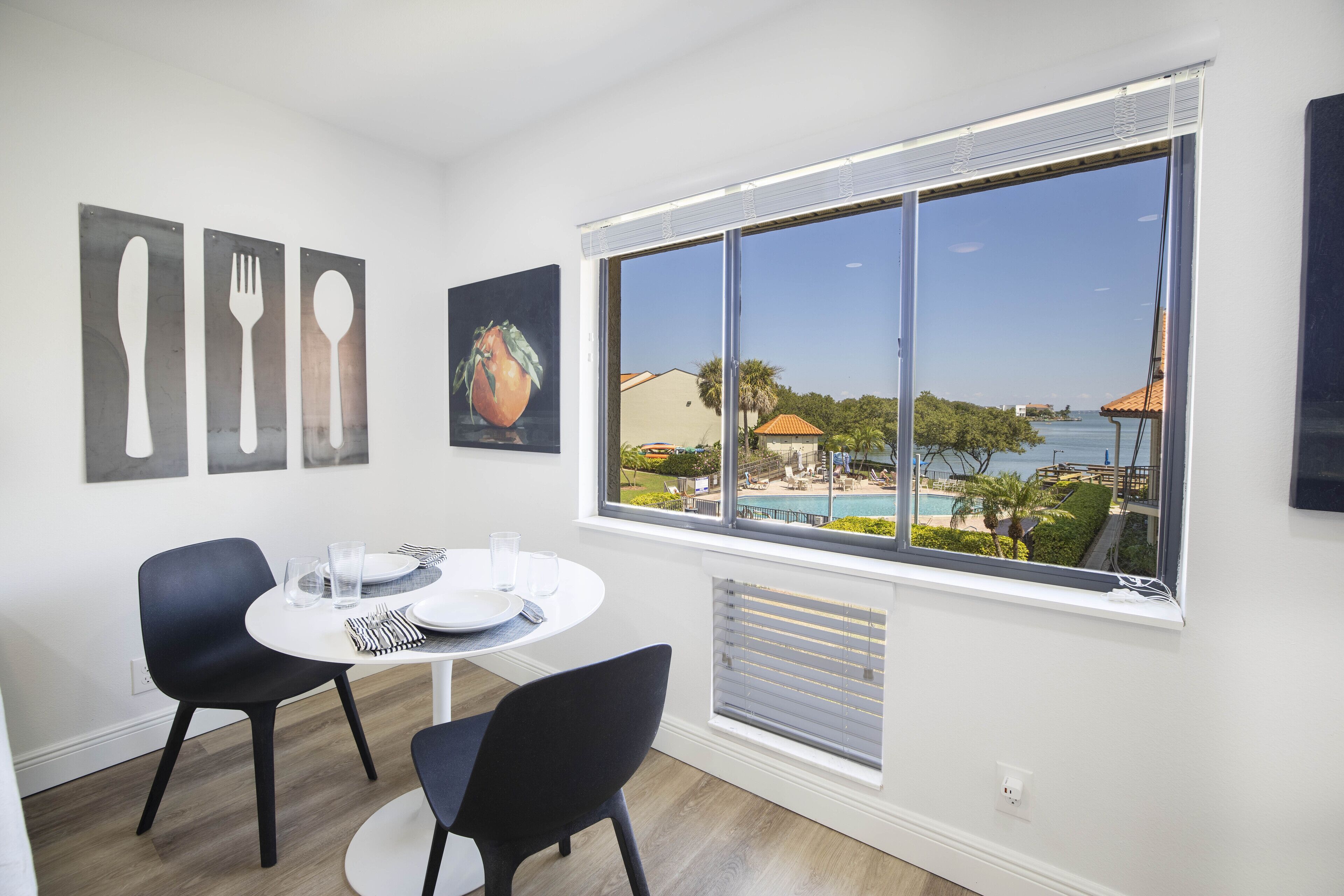 A dining area with a round table, two chairs, and a view of a pool and buildings through a large window.