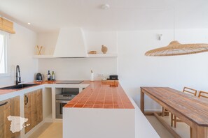 Una cocina moderna con una isla central, una mesa de comedor y una lámpara colgante.