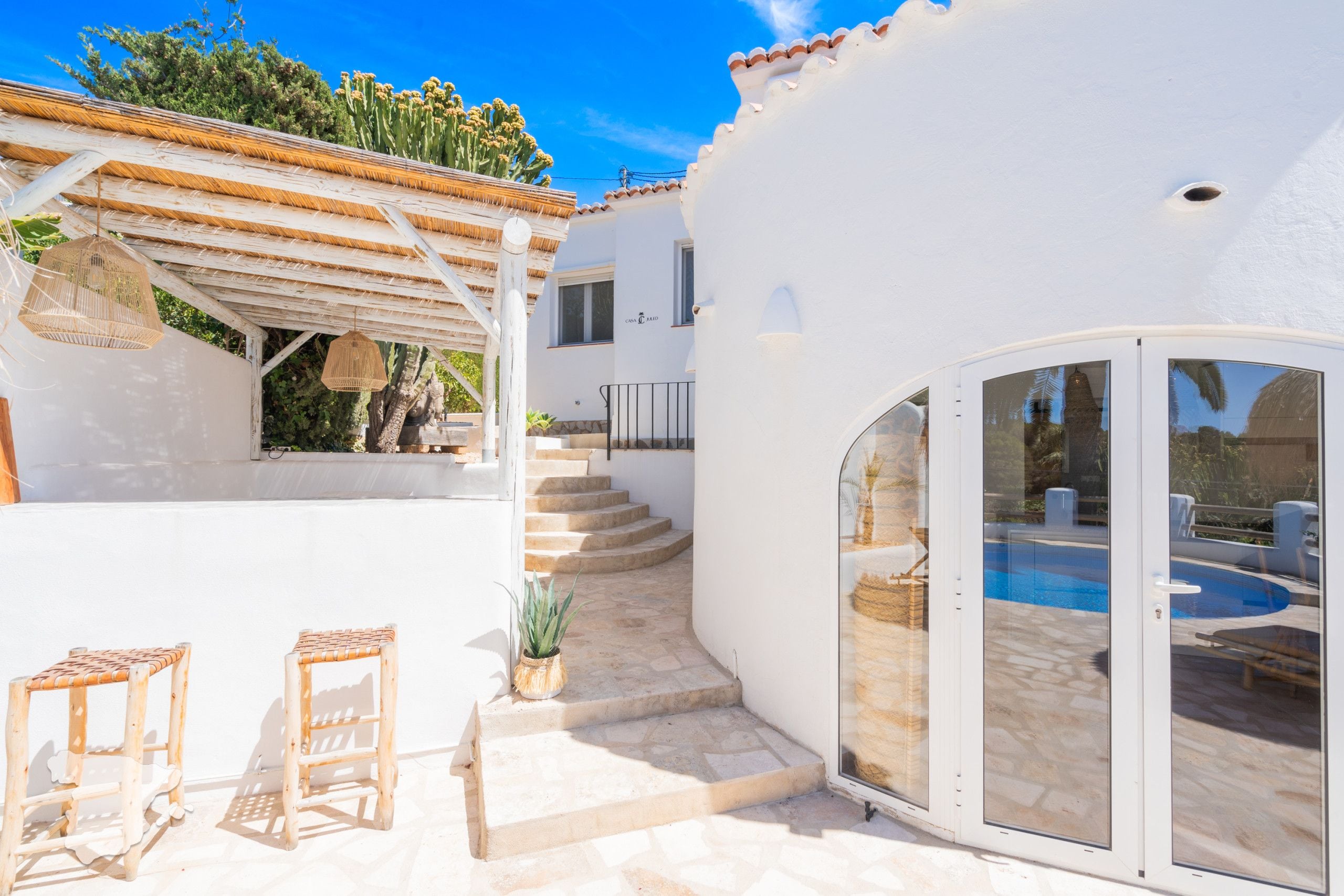 A white villa with a pool, a covered patio, and a staircase leading to the upper floor.
