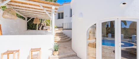 A white villa with a pool, a covered patio, and a staircase leading to the upper floor.