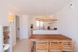 Une cuisine moderne avec une table et des chaises en bois, un luminaire suspendu et une vue sur le salon attenant.