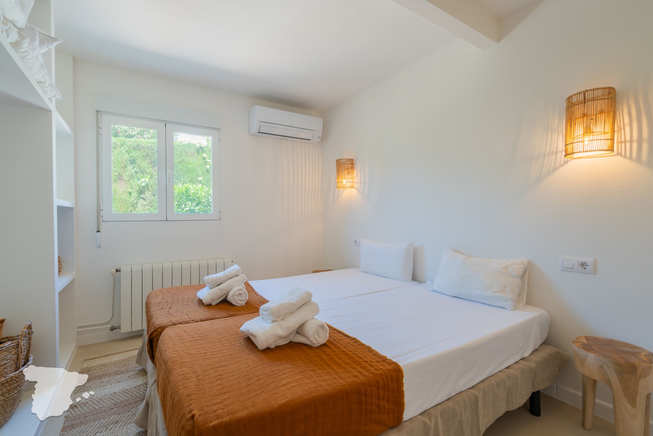 Een hotelkamer met twee bedden, een raam, een airconditioning en een wandlamp.