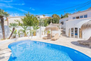 Una piscina con sillas de descanso, rodeada de edificios blancos y palmeras.