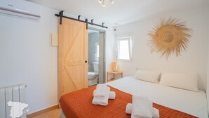 A hotel room with a bed, a bathroom, a sliding door, a wall-mounted light fixture, and a decorative sun-like wall art piece. - CostaBlancaDreams - Casa Juleo in Benissa (Benissa)