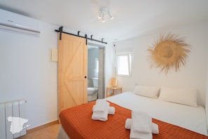 A hotel room with a bed, a bathroom, a sliding door, a wall-mounted light fixture, and a decorative sun-like wall art piece. - CostaBlancaDreams - Casa Juleo in Benissa (Benissa)