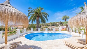 A swimming pool with lounge chairs and thatched umbrellas, surrounded by palm trees and a white fence. - CostaBlancaDreams - Casa Juleo in Benissa (Benissa)