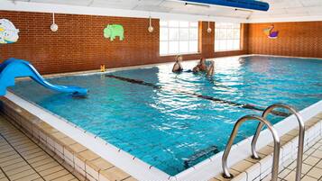 Piscina interna com um escorregador azul, parede de tijolos com murais de animais e chão de azulejos.