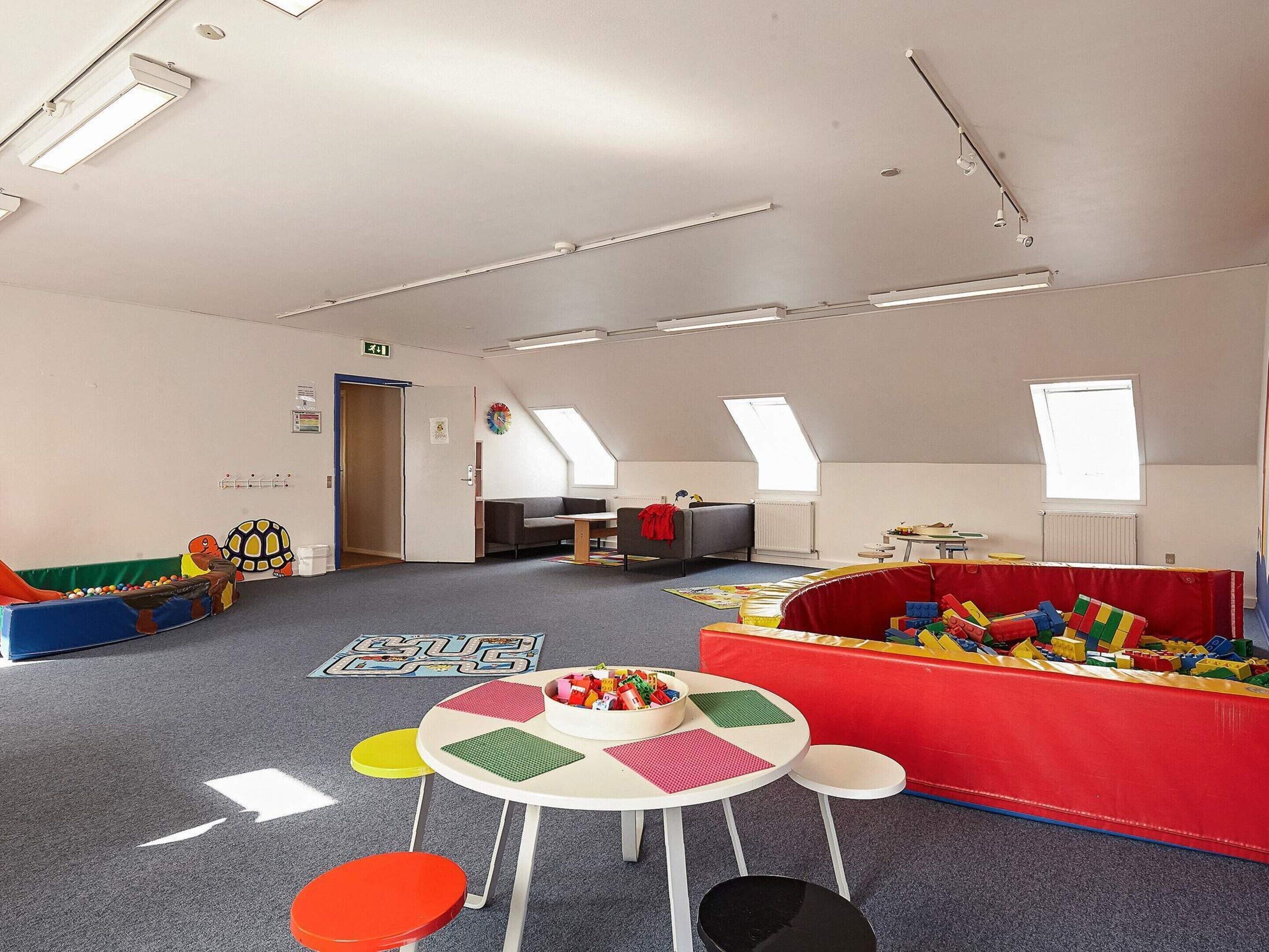Una sala de juegos infantil con techo alto, tragaluces y diversas estructuras y mesas para jugar.