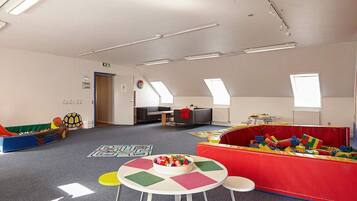 Una sala de juegos infantil con techo alto, tragaluces y diversas estructuras y mesas para jugar.