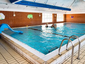 En inomhuspool med en blå vattenrutschkana, en tegelvägg och ett tak med ventilationskanaler.