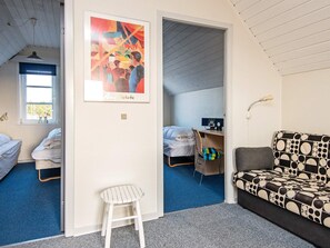 A room with two beds, a chair, a sofa, a poster, and a desk with a chair.