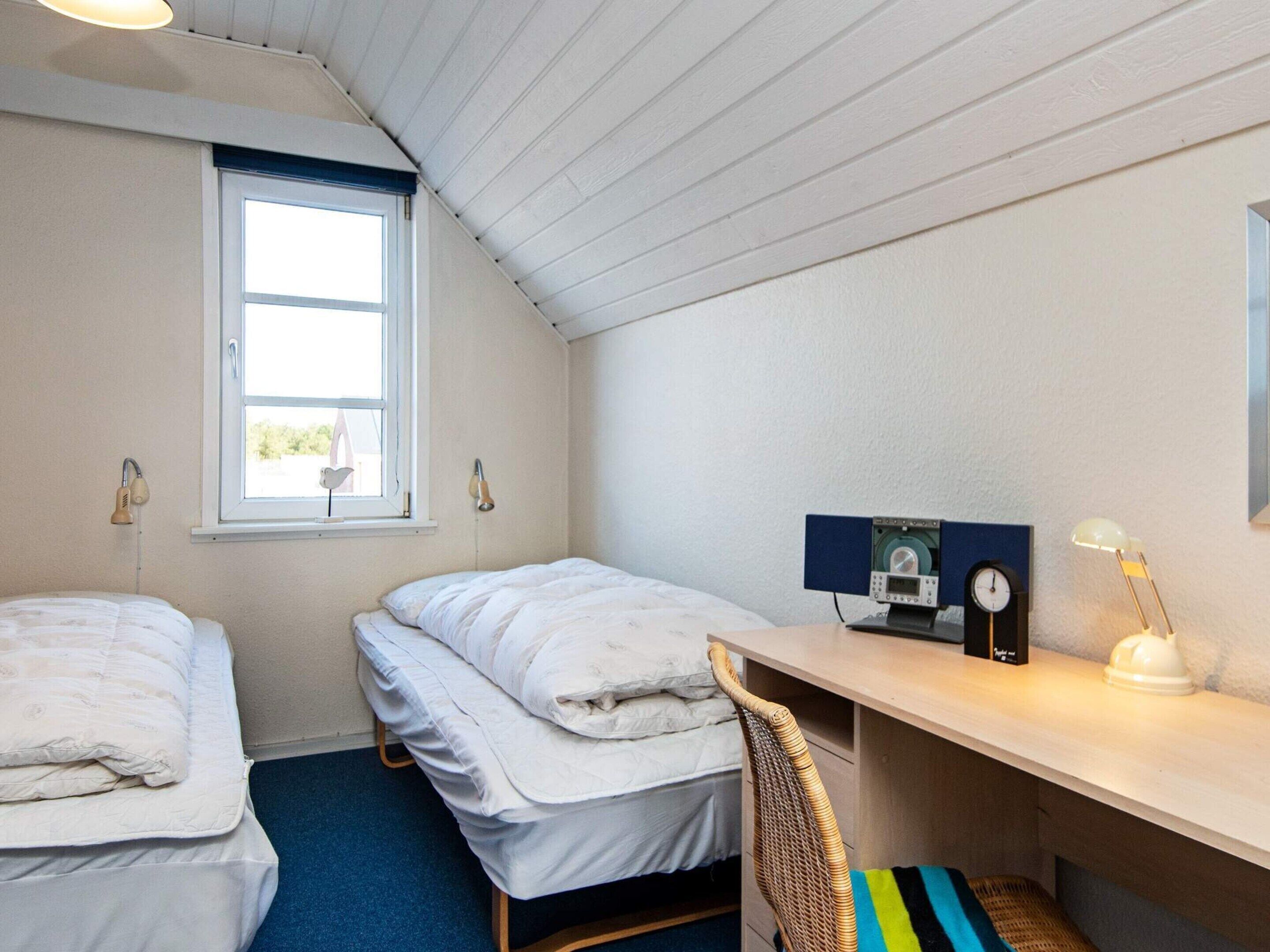 A small, tidy room with two single beds, a desk with a chair, a window, and a wall-mounted clock.