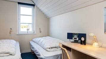 A small, tidy room with two single beds, a desk with a chair, a window, and a wall-mounted clock.