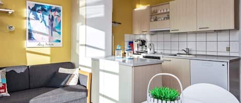 A compact living space with a kitchenette, a grey sofa, a small dining table, and a white cabinet.